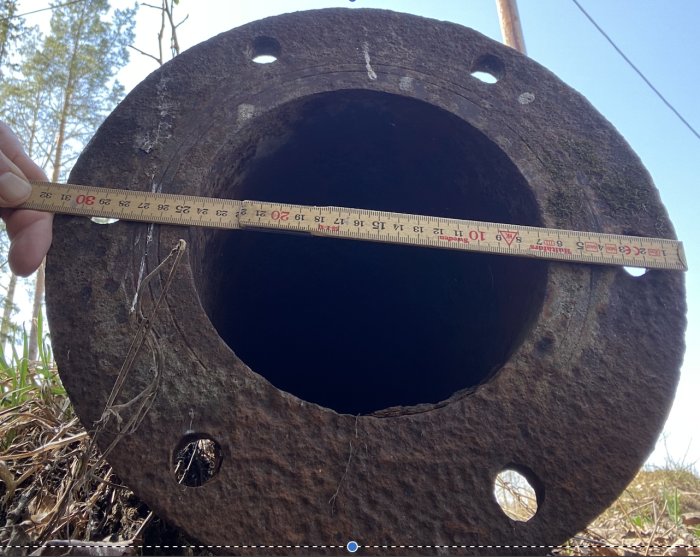 Måttband visar diameter på rostig metallisk struktur mot himlen.