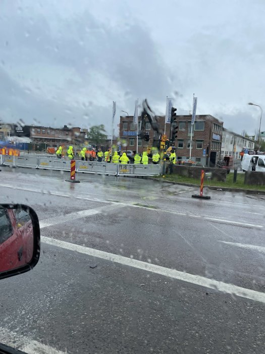 Grupp människor i hög synlighet kläder, regnig väg, trafikljus, stadsmiljö, synlig bil spegel, våt vindruta.