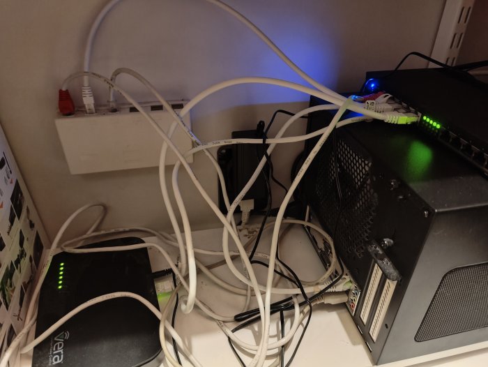 Rörig samling av nätverksutrustning och kablar, inklusive router, modem och datorer.