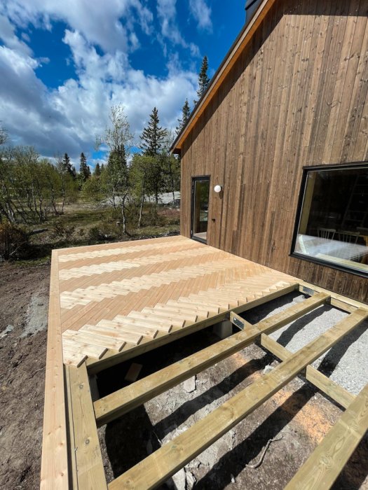 Trätrall under konstruktion, modernt trähus, blå himmel med moln, naturskönt, dagtid.