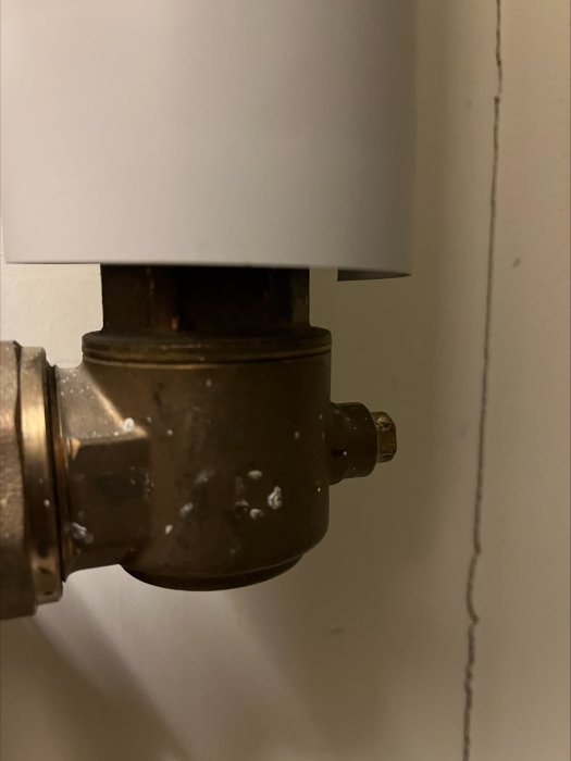 Närbild på en äldre termostatventil till en radiator, mot en vit vägg.