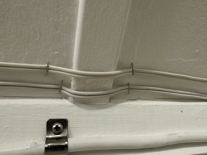 Vita kablar fastsatta längs vägg och list med metallklämmor och en skruvfast kabelklämma.