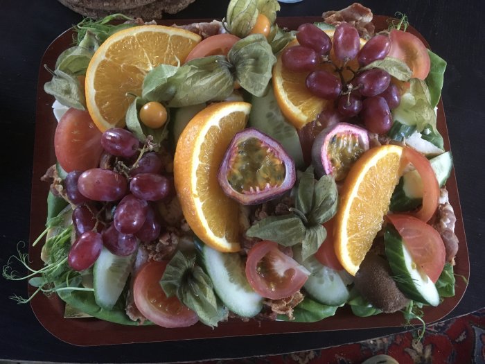 Ett färgrikt fat med frukt och grönsaker: apelsin, passionsfrukt, vindruvor, kiwi, tomat och grönsallad.