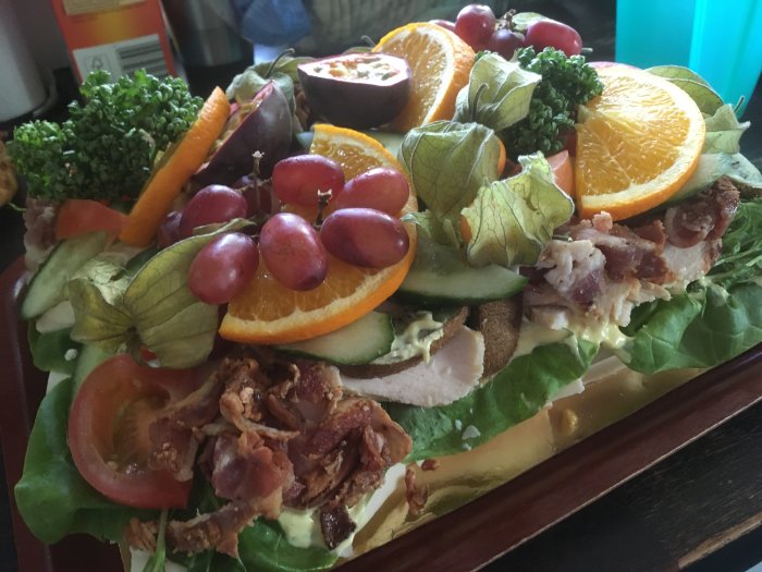 Macka med kyckling, bacon, grönsaker, grönt, apelsinskivor och druvor. Färgrik, matpresentation, uppdukad på träfat.