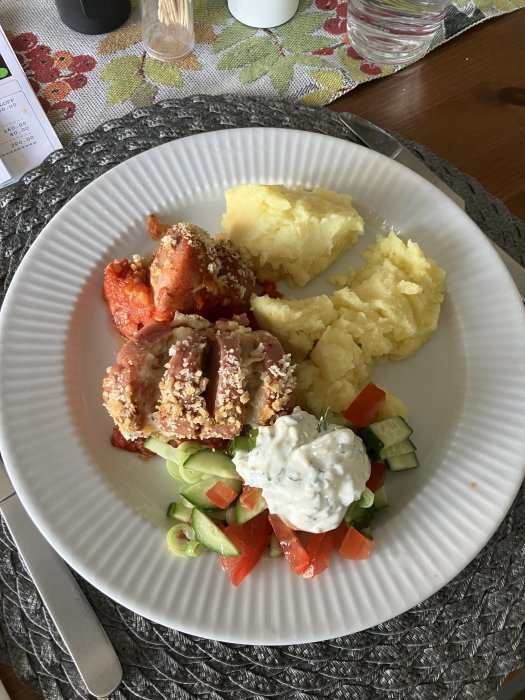 En tallrik med mat: potatismos, sallad, krispig kyckling och tzatziki. Hemlagad måltid på bord.