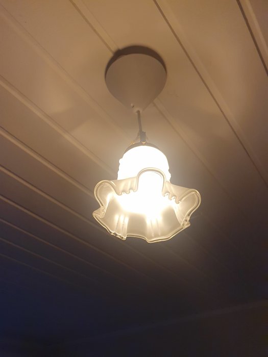 Takmonterad lampa med klassisk design, tänd, ger mjuk belysning, mot vit innertakspanel.