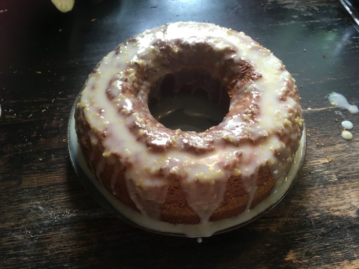 Sockerkaka med glasyr på mörkt träbord, bitar av skal syns, smulor, hemlagat bakverk.