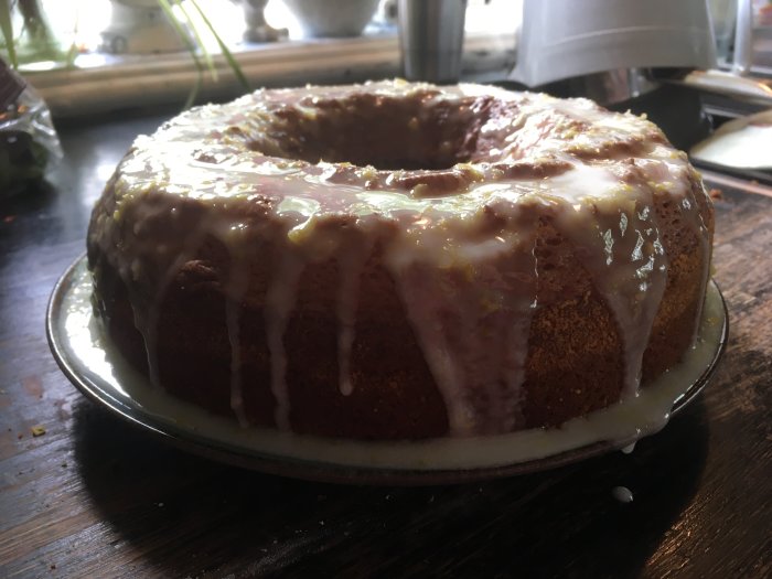 Bundtkaka med vit glasyr på fat, inomhusbelysning, mörk bakgrund, närbild.