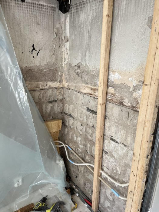 En pågående renovering visar blottlagda väggar, isolering, rör, verktyg och en plastskynke.