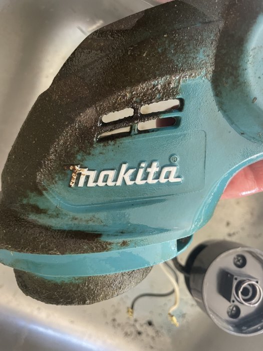 Slitet Makita-verktyg med smuts och rester, blågrön färg, närbild, delvis klippta kablar, oanvänt skick.