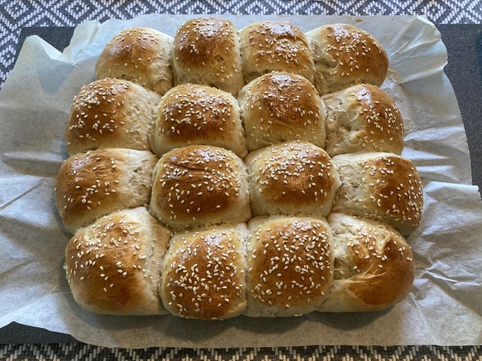 Nybakade frallor på pappersunderlägg, sammankopplade i rutmönster, strösslade med sesamfrön.