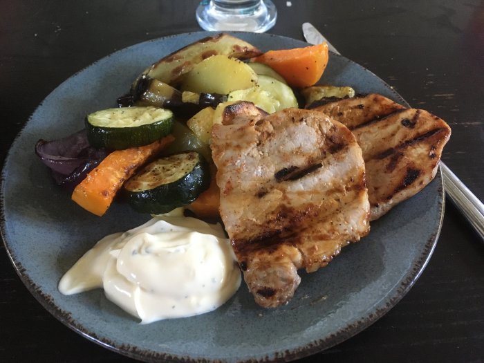 Grillat kött med rostade grönsaker och vitlöksås på blå tallrik.
