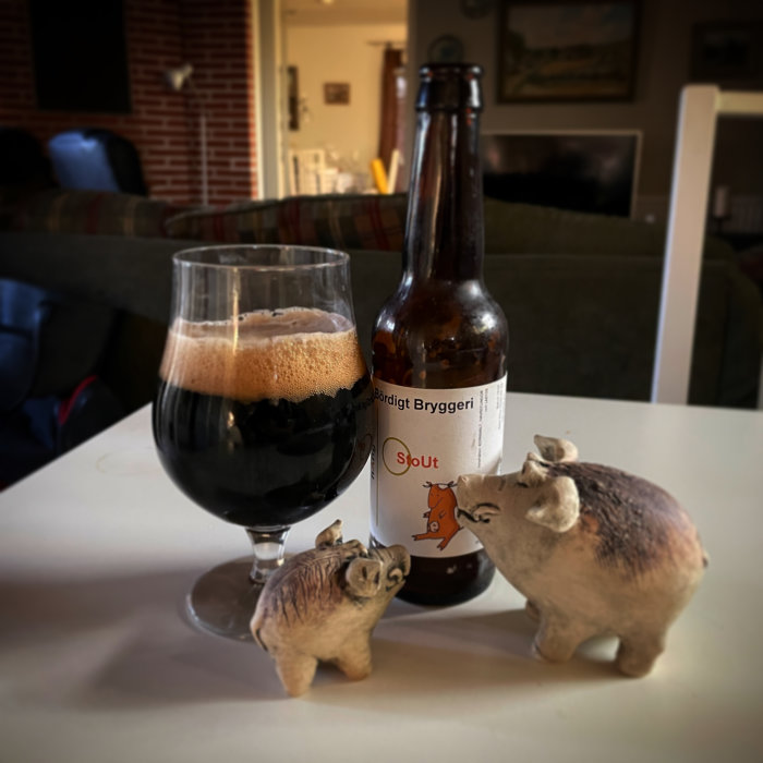 Ett ölglas fyllt med stout nära en tom flaska och två prydnadsgrisar på ett bord.