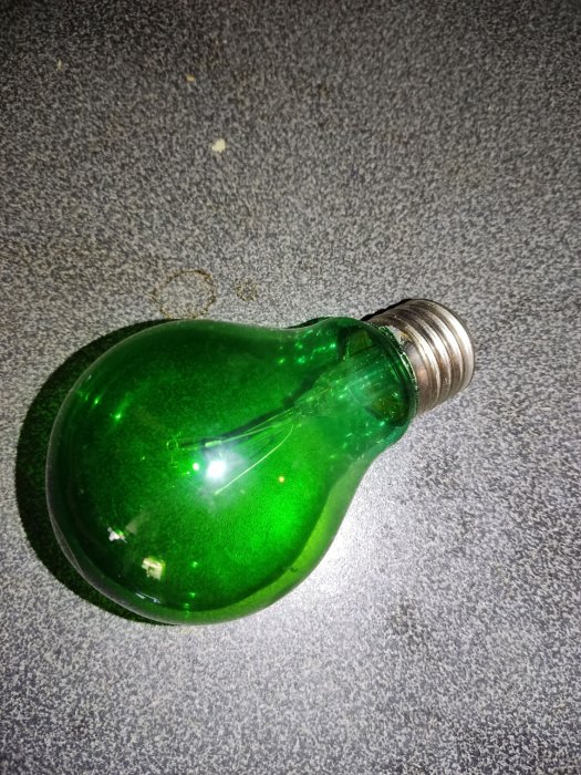 Grön glödlampa ligger på en grå texturerad yta, ovanifrån perspektiv.