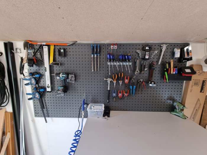 Verkstadsvägg med verktygstavla, organiserade verktyg, skruvmejslar, tänger, borr, nycklar, måttband och arbetsbänk.