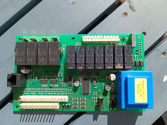 Elektronikkort med reläer och kretsar, industristyrning, blå transformator, på träyta i dagsljus.