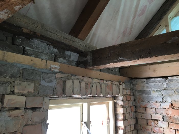 Renovering pågår, exponerade tegelväggar, träbjälkar, isolering synlig, ofärdig konstruktion, inomhus, byggprocess.