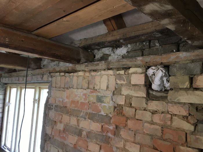 Renoveringsarbete, murat tegel, träbjälkar, delvis rivet tak, gammal byggnad, oavslutad konstruktion, synlig isolering.