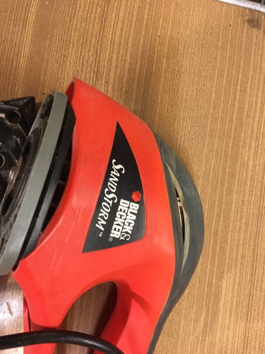 Röd Black & Decker slipmaskin på ett brunt underlag.