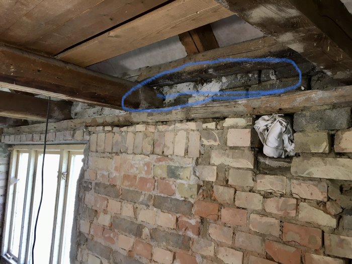 Renoveringsarbete pågår, tegelvägg och träbjälklag med blå märkningar och fyllning i öppning.