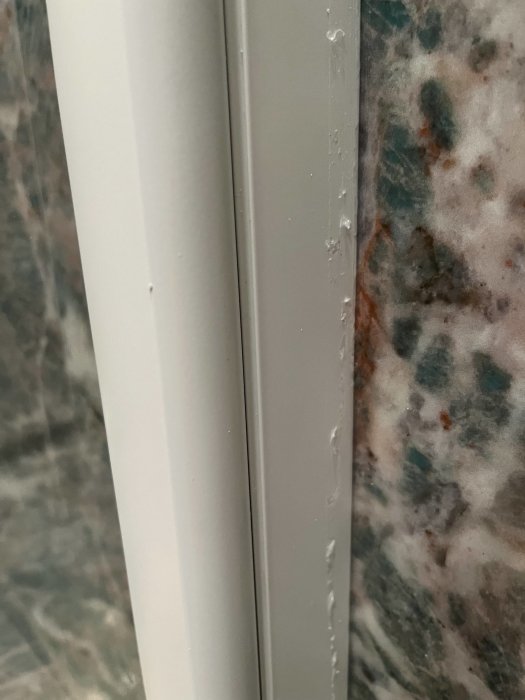 Vit dörrkarm med vattendroppar, marmorerad grön och beige vägg i bakgrunden.