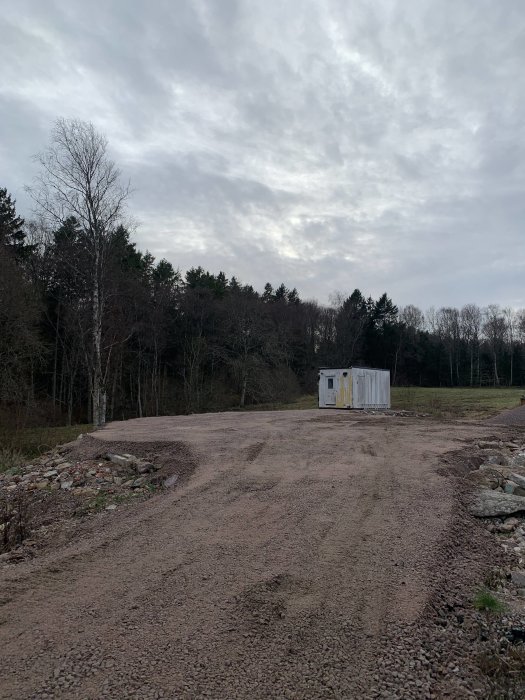 Öde byggarbetsplats, grusväg, skogsbakgrund, mulet, container, ingen aktivitet, dagtid.