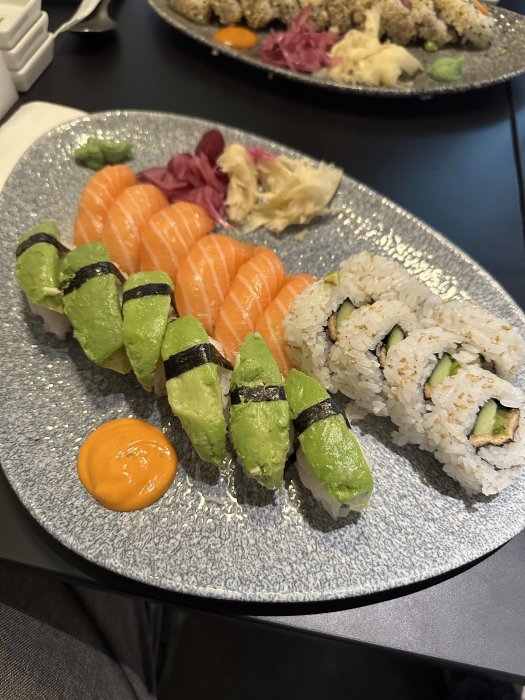 En tallrik med färsk sushi, inklusive lax nigiri, avokadomaki, ingefära, wasabi och dippås.