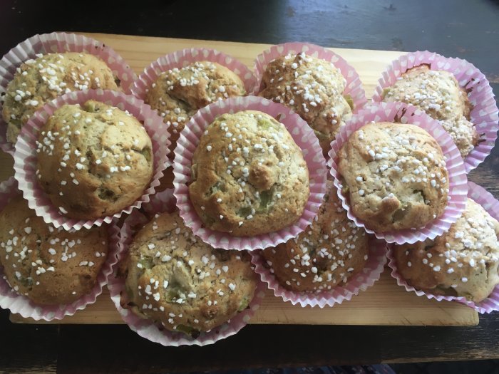 Flera nybakade muffins med pärlsocker på träskärbräda. Söta bakverk i rosa formar.
