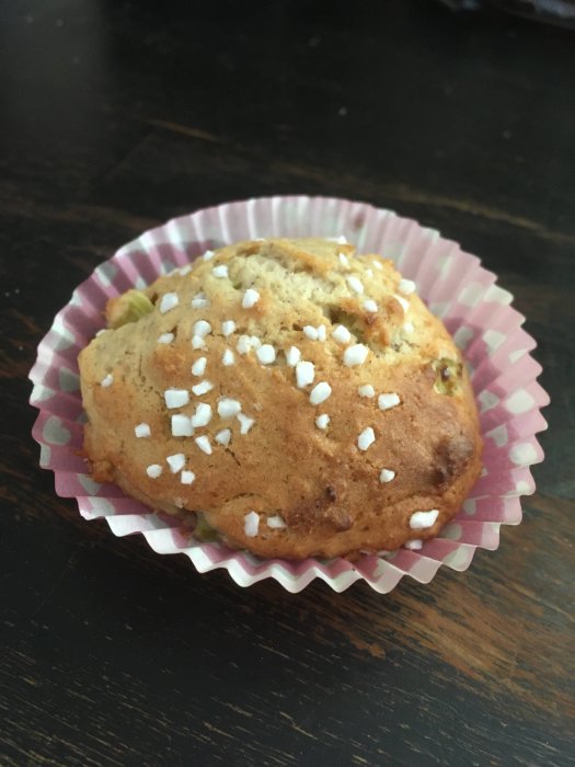 En muffin med pärlsocker på toppen i ett rosa-randigt muffinsform står på mörkt bord.