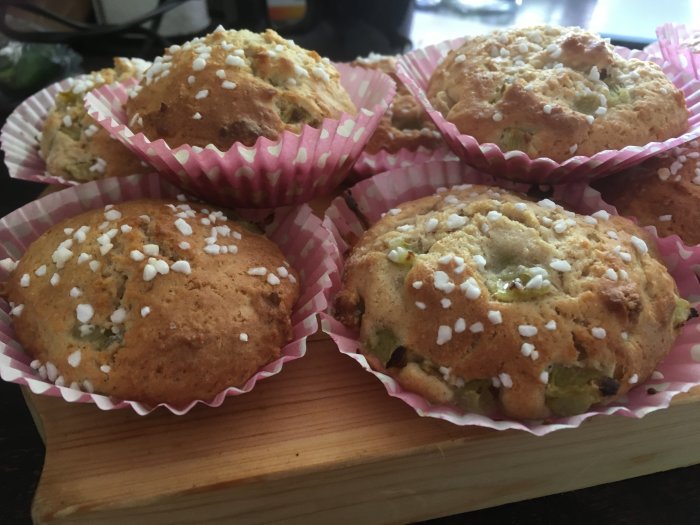 Färska muffins med pärlsocker på träskärbräda, rosa och vita formar.