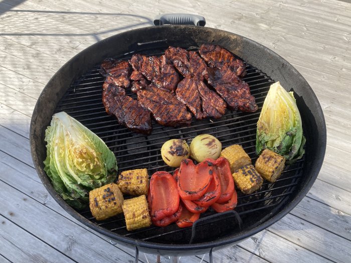 Kolgrill med kött och grönsaker: majs, sallad, röd paprika och lökar på träaltan.