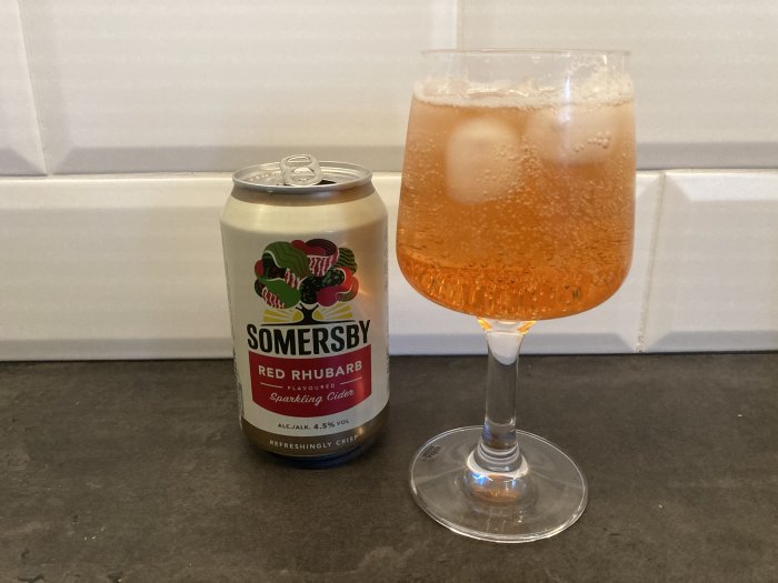 Somersby Red Rhubarb cider burk, bubblig dryck i glas, isbitar, köksbänk, kakelvägg.