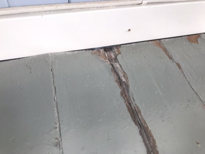 Skadat trägolv vid dörrtröskel med synlig fukt- eller vattenskada.