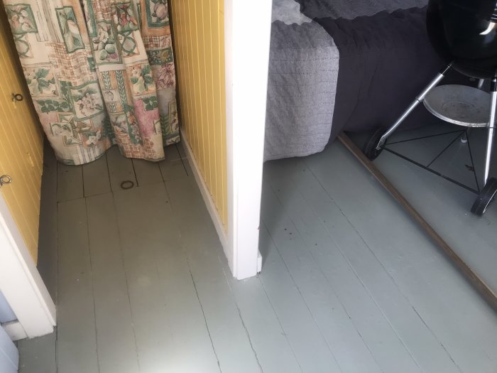 Ett hörn av ett rum med grått golv, gardin, dörrkarm och grill.