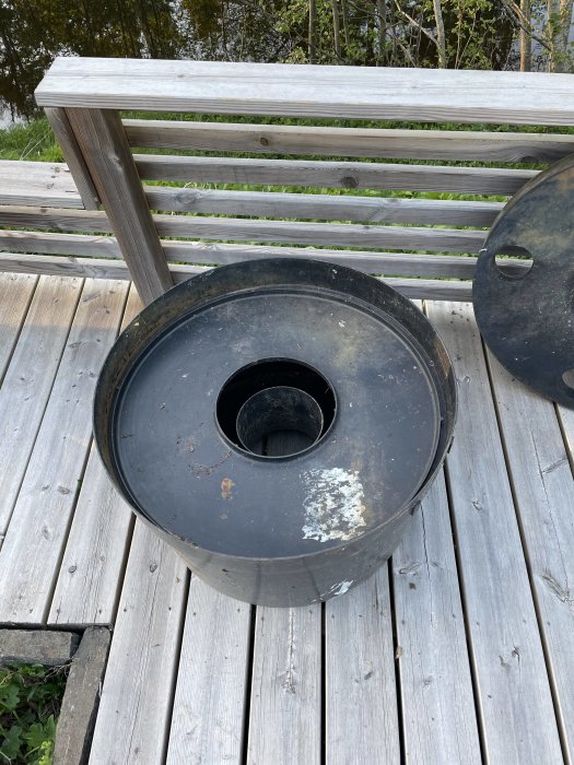 En svart soptunna på ett träaltandäck nära en parkbänk, omgiven av natur.