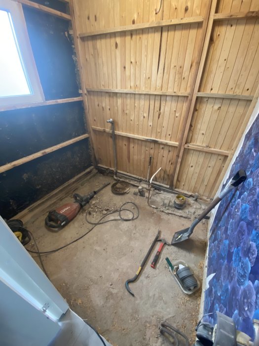 Byggarbetsplats med träväggar, verktyg på golvet, öppet fönster och avslitet tyg till höger.