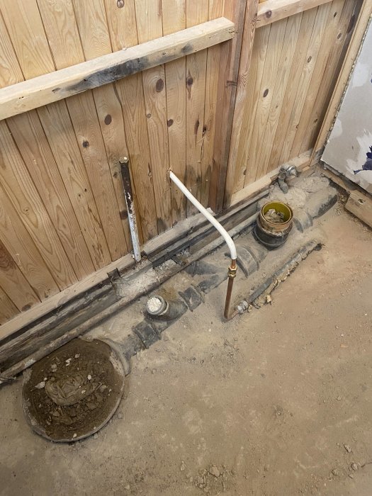 Renoveringsplats, avtappningsrör, betonggolv, träväggar, öppen golvyta, installationsarbete pågår.
