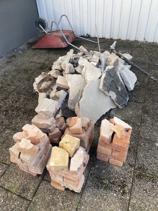 Hög av trasiga tegelstenar och betong, röd skottkärra och verktyg på grus och gräs. Renovering eller rivning.
