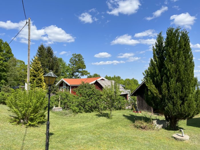 Idyllisk landsbygdsträdgård med röda hus, gröna träd, klarblå himmel och en gammal lyktstolpe.