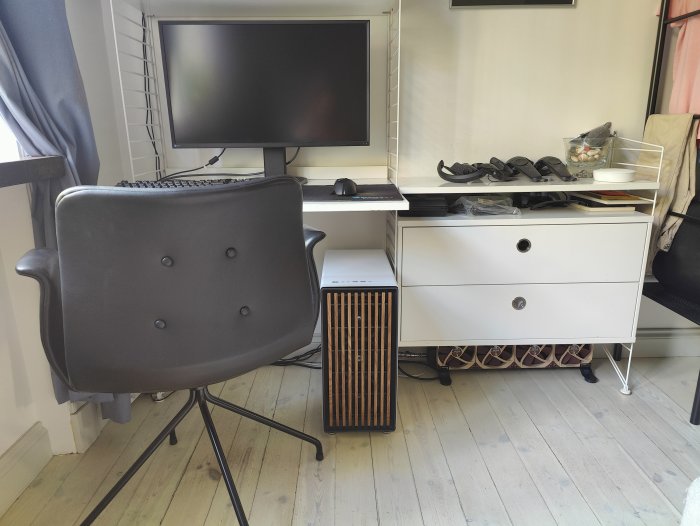 Ett hemmakontor med stol, skrivbord, datorskärm, tangentbord och personliga föremål.