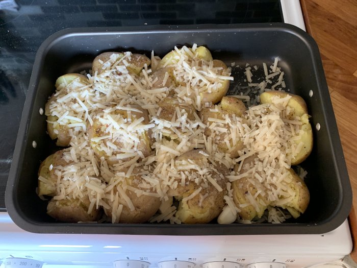 Potatis för gratäng med ost ovanpå, i ugnssäker form, förberedd för matlagning.