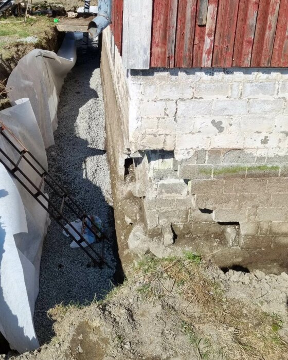 Grundläggning arbete vid hus, grusfyllning vid fundament, skadade tegelväggar, armeringsjärn, soligt.