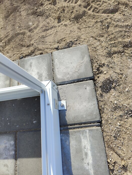 Vit metallram vid övergång mellan betongplattor och sandig mark.