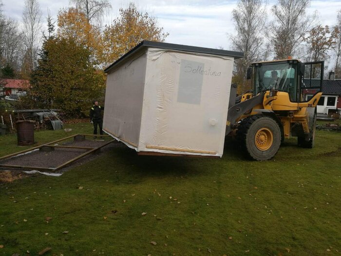 Flytt av modulärt skrymsle, gaffeltruck, person, gräs, höstlöv, hus bakgrund, övergivet.