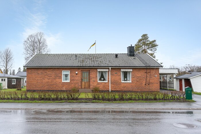 Enfamiljshus i tegel, svenskt villaområde, svensk flagga, molnig dag, fönster, brevlåda, vått efter regn.