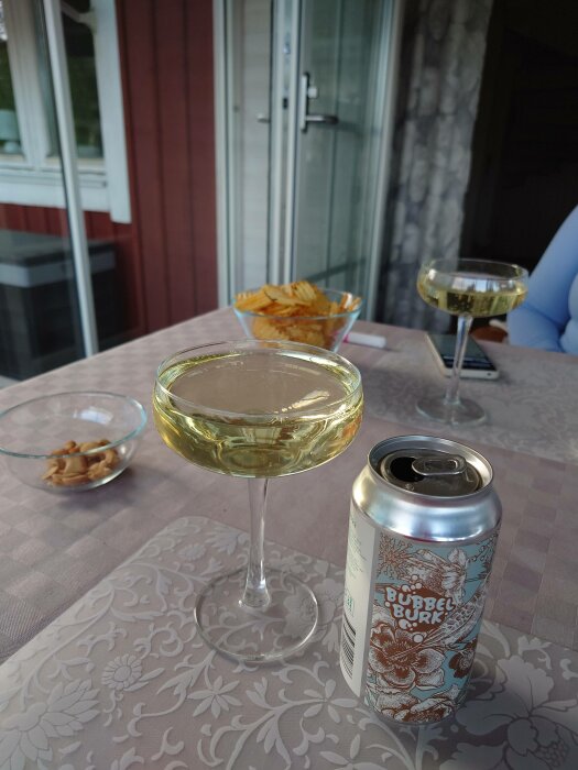 Utomhusmingel med dryck i glas, burköl, snacks, och en person vid ett bord.