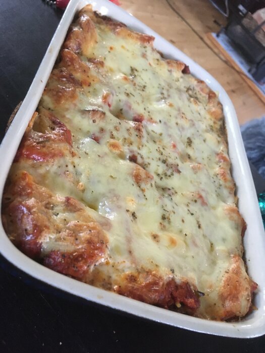 Gratinerad lasagne i vit form, gyllenbrun ost, tomat, örter på toppen.
