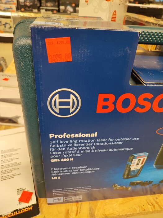 Förpackning av Bosch Professional rotationslaser med pris och beskrivande text på olika språk.