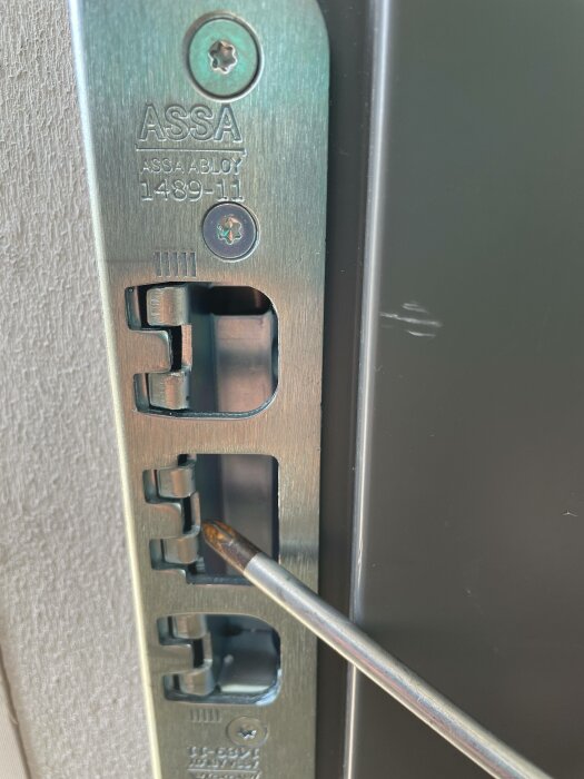 Låskista märkt "ASSA ABLOY", skruvmejsel installerar eller justerar låsmekanism, säkerhetsdetalj, dörrmontering.