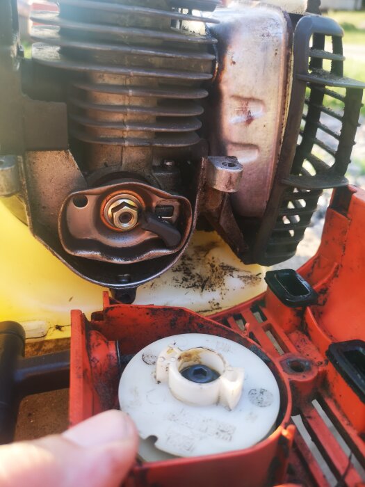 Motor till motorsåg delvis isärmonterad, smutsig, underhåll eller reparation, utomhus.